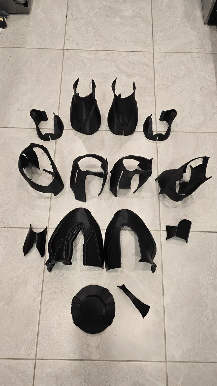 Sixteen black 3D printed cosplay armor shell pieces laid out