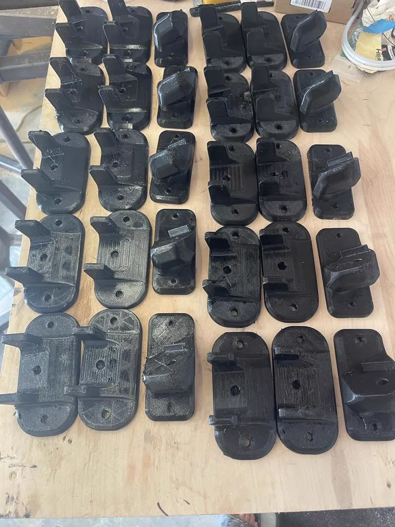 Batch of thirty black 3D printed mounting brackets on a workbench