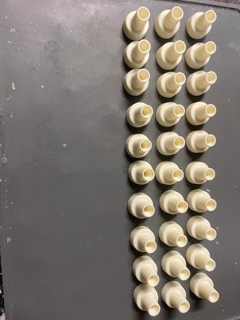Grid of thirty cream 3D printed threaded nozzle adapter fittings