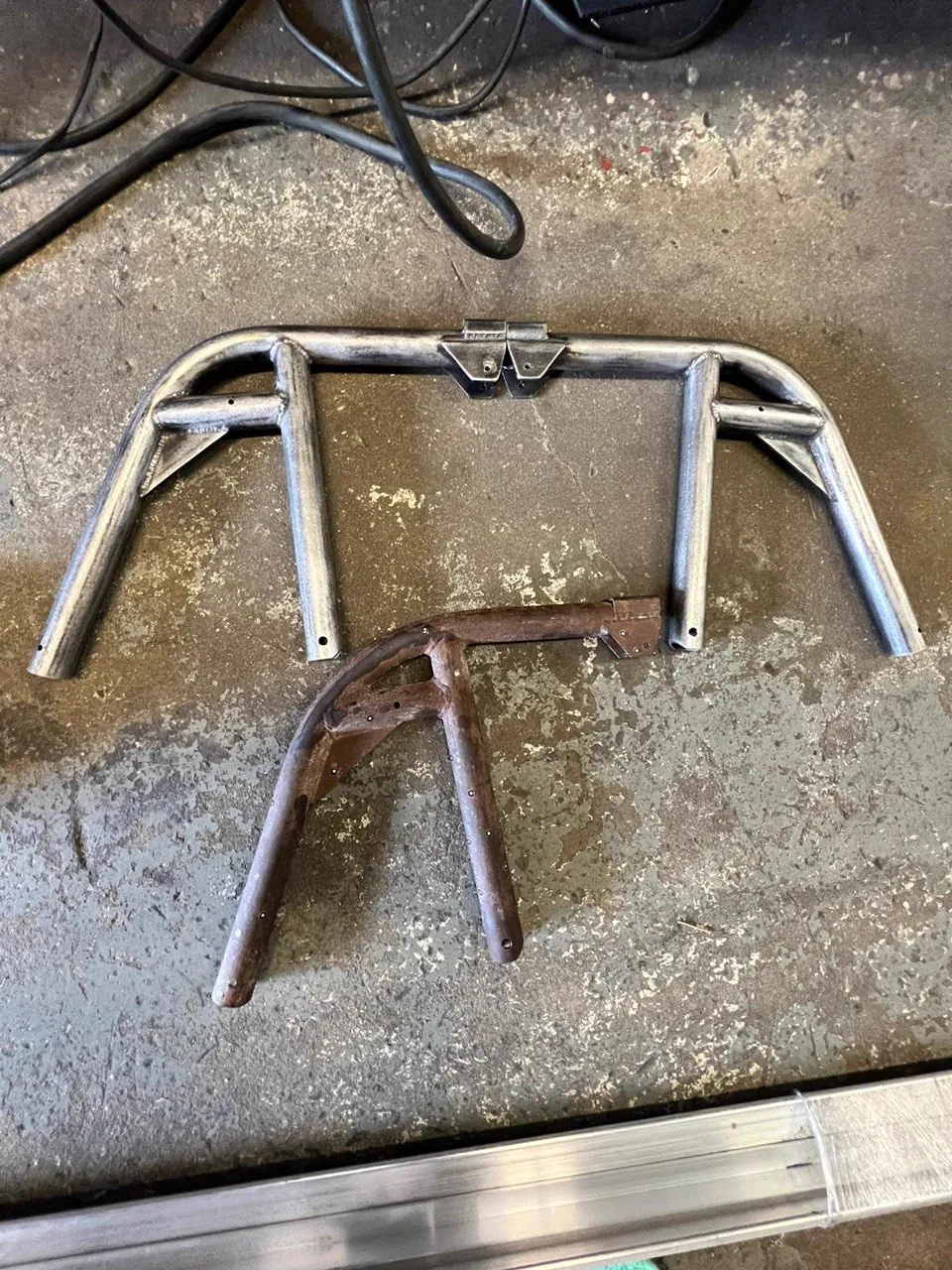 Rusted original roll bar bracket beside the newly fabricated bright metal recreation